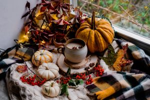 Cozy autumnal Pumpkin latte scene by the window with autumn leaves, pumpkins, knits and hot drink