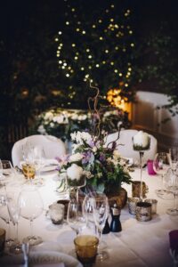 A table laid for a special occasion, with a floral centrepiece and candles, at night.