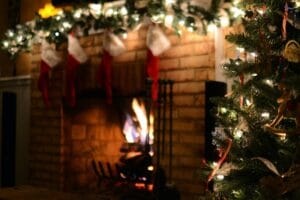 A traditionally decorated Christmas tree in front of a fire place with a fire and decorated mantle